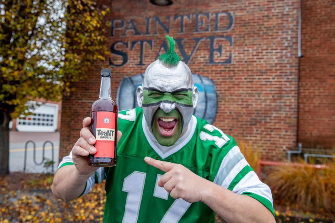 The Philly Sports Guy in front of Painted Stave Distillery, holding a bottle of TeaNT Dynomite Sweet Tea Liqueur